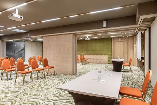 Un salón de conferencias con una gran mesa, sillas anaranjadas, un proyector y una alfombra estampada.