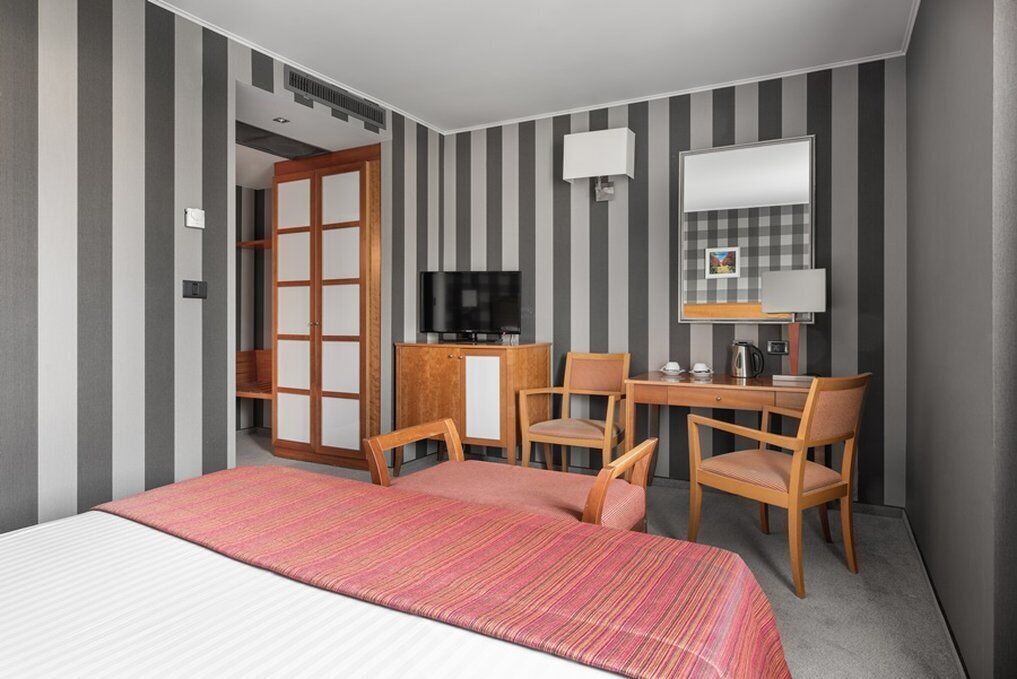 A hotel room with a bed, a desk with a chair, a television, and a wardrobe.