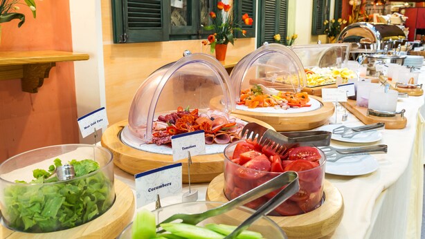 Een buffet met aangegeven secties voor vleeswaren, tomaten, komkommers en andere groenten.
