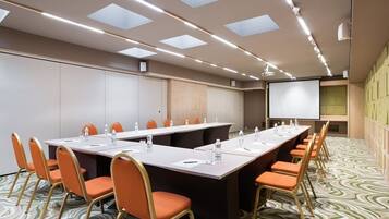 A conference room with a long table, orange chairs, a projector screen, and a patterned carpet.