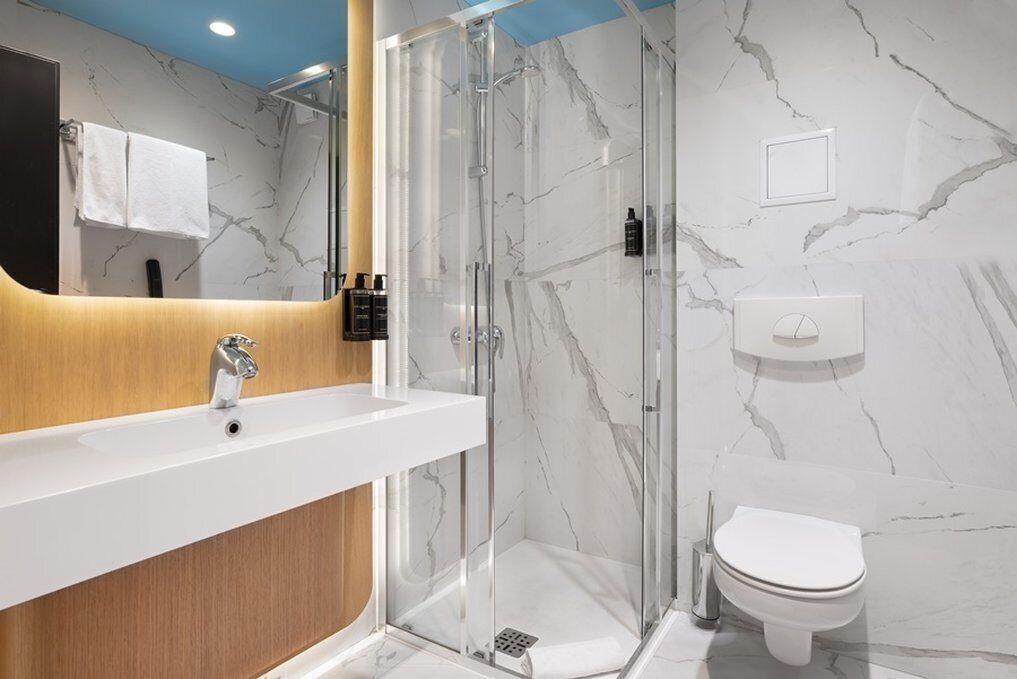 Een moderne badkamer met een marmeren wand, een houten wastafelmeubel, een douchecabine van glas en een wit toilet.