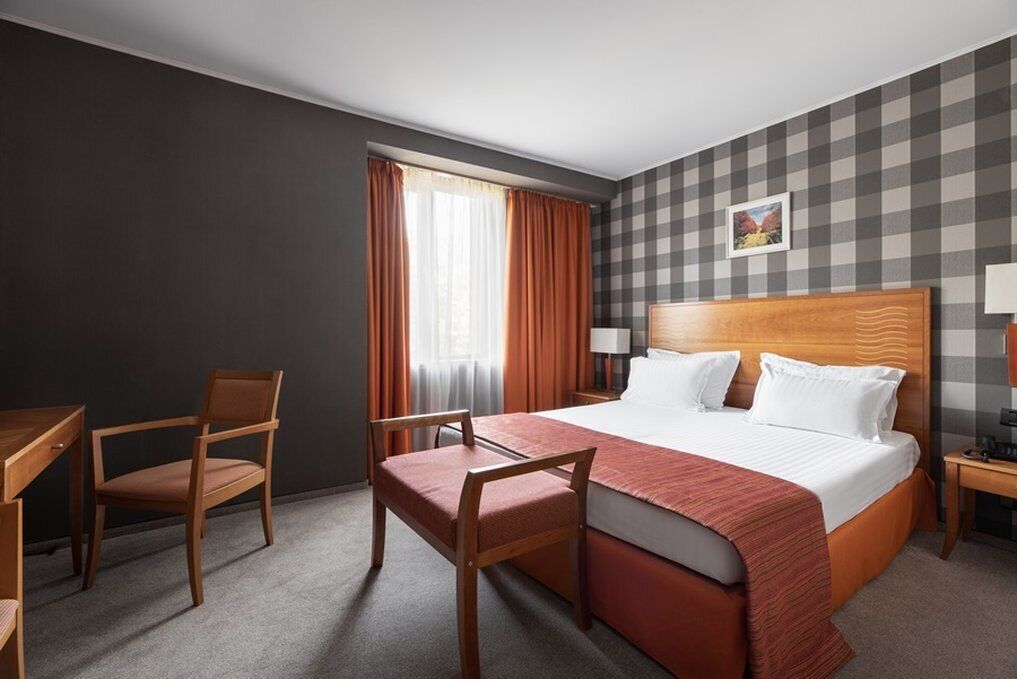 Una habitación de hotel con una cama grande, dos sillas, un escritorio y una mesita de noche.