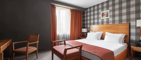 A hotel room with a large bed, two chairs, a desk, and a nightstand.