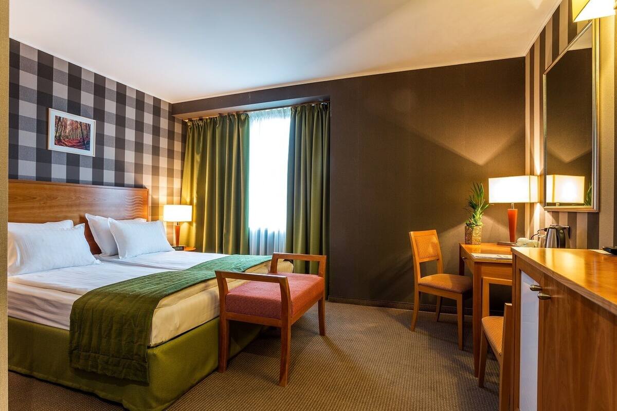 Een hotelkamer met een bed, twee stoelen, een bureau, een lamp en een spiegel.