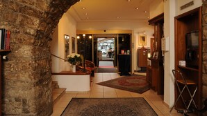 Un hall d’hôtel avec une arche en pierre, un comptoir d’accueil, un distributeur de café et une vue sur la rue.