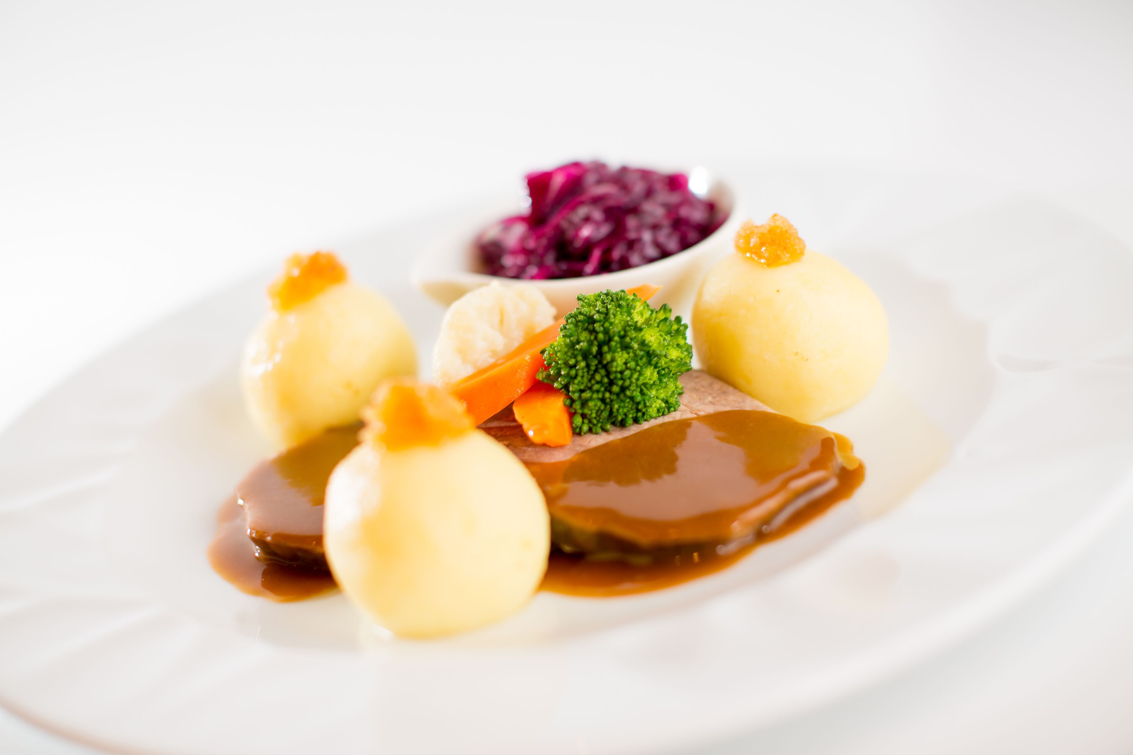 Ein Teller mit Knödeln, Fleisch, Gemüse und einer kleinen Schüssel Rotkohl.