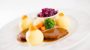 Ein Teller mit Knödeln, Fleisch, Gemüse und einer kleinen Schüssel Rotkohl.