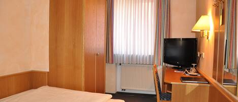 Une chambre d’hôtel avec un lit, un bureau avec une télévision, une chaise et une fenêtre avec des rideaux.