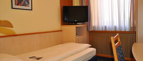 A hotel room with a single bed, a television on a wooden stand, a small table, and a chair.
