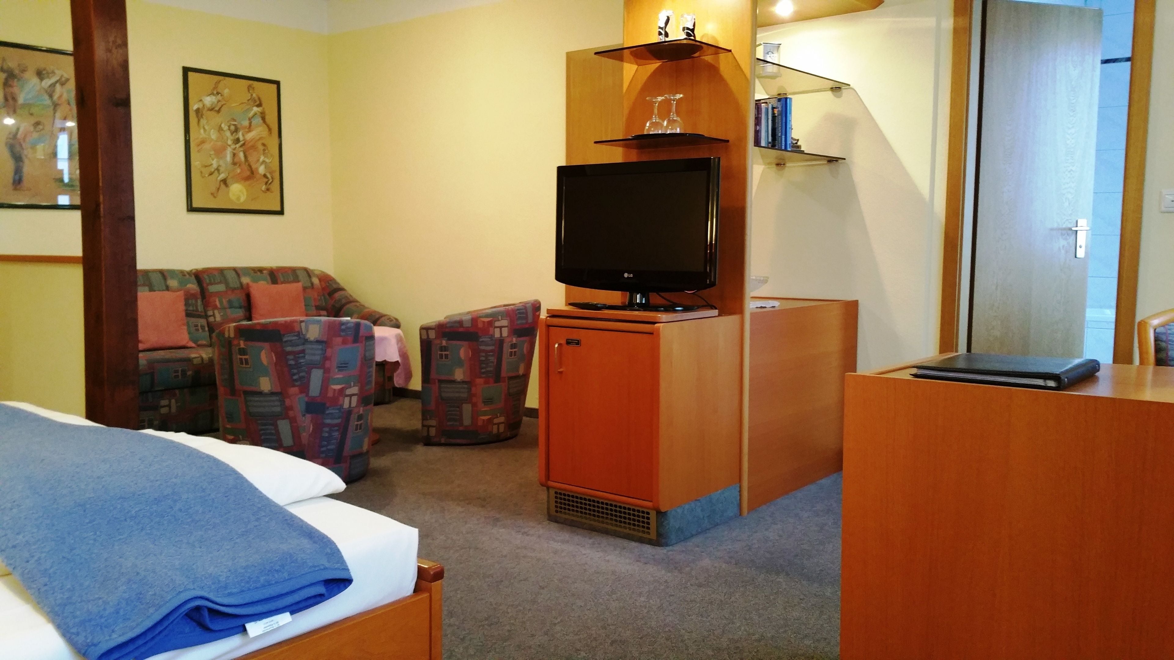 Une chambre d’hôtel comprenant un lit, un bureau avec un téléviseur à écran plat, un petit meuble de rangement, un canapé et une chaise.
