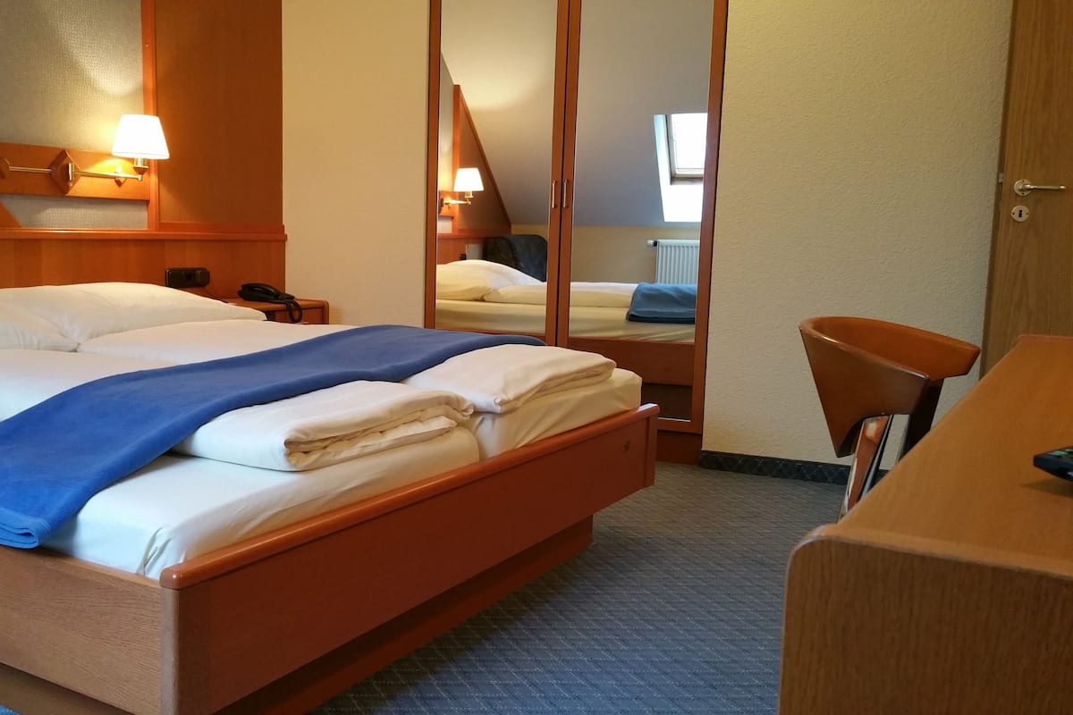 Une chambre d’hôtel avec un grand lit, un bureau, une chaise, un miroir et une fenêtre.