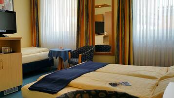 A hotel room with a bed, a desk with a chair, a television, and a window with curtains.