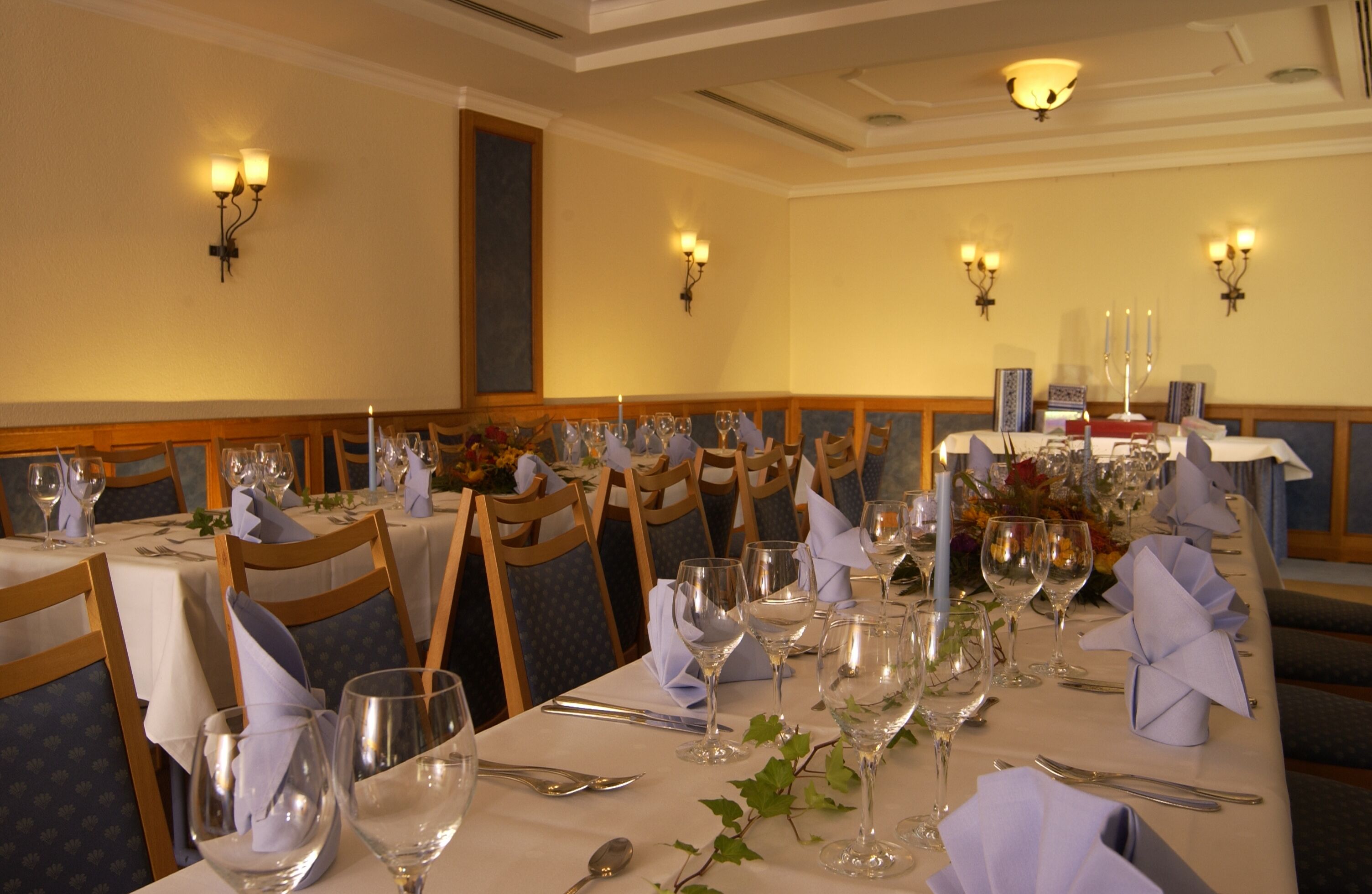 A formal dining room with tables set for a meal, featuring white tablecloths, neatly arranged silverware, and glassware.