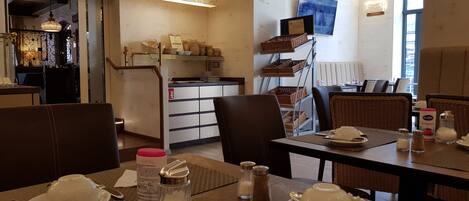 A restaurant with tables set for dining, a kitchen area, and a television mounted on the wall.