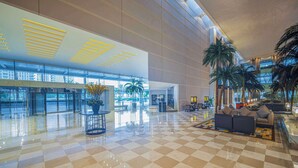 Um hall amplo com piso xadrez, área de estar com sofás e uma grande planta.