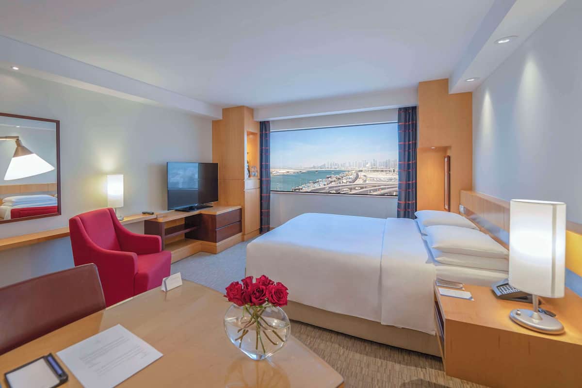A hotel room with a bed, a desk, a chair, a TV, and a view of a cityscape.