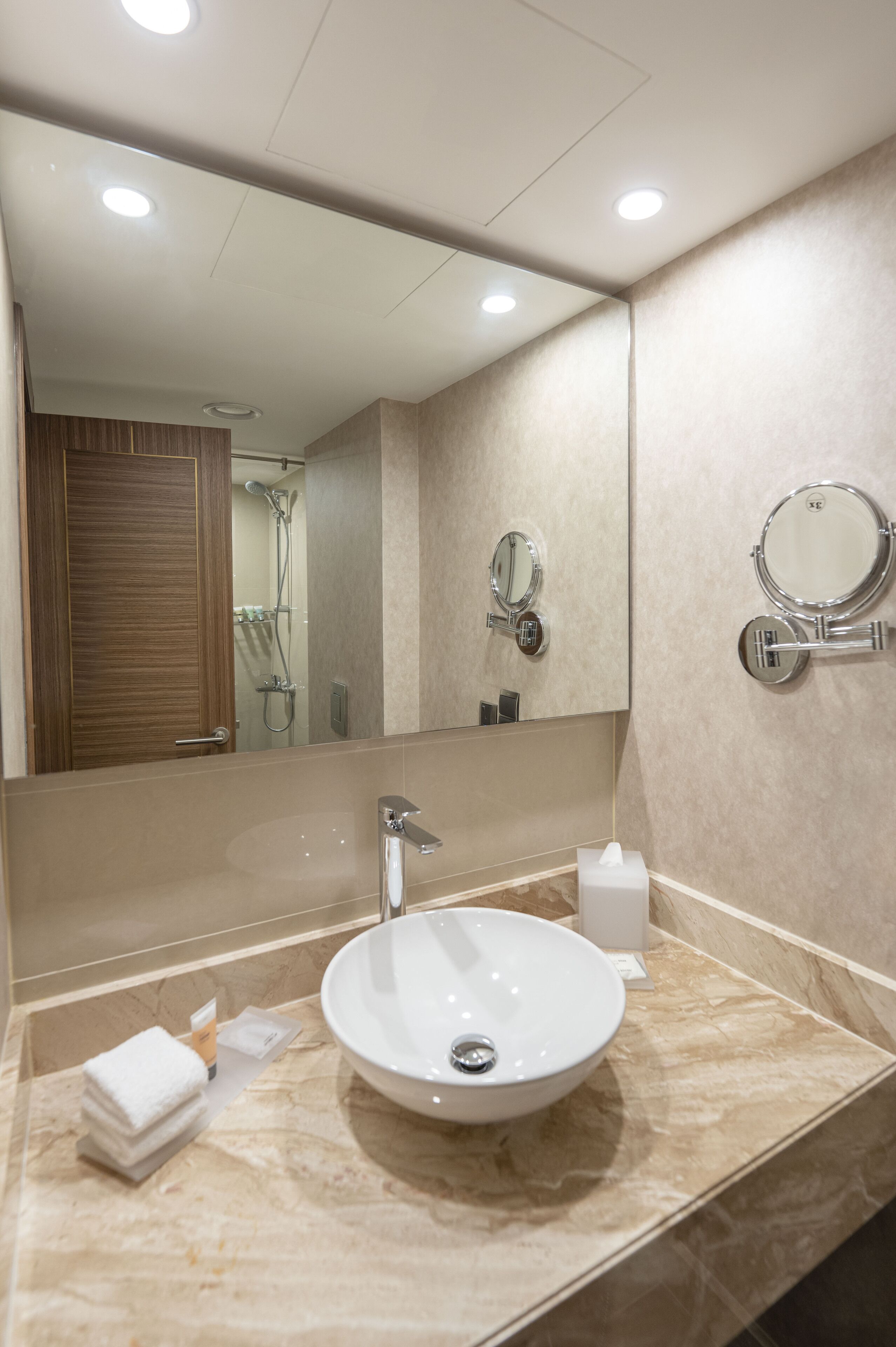 Un baño moderno con un espejo grande, un espejo redondo en la pared, un lavamanos blanco y un dispensador de toallas.