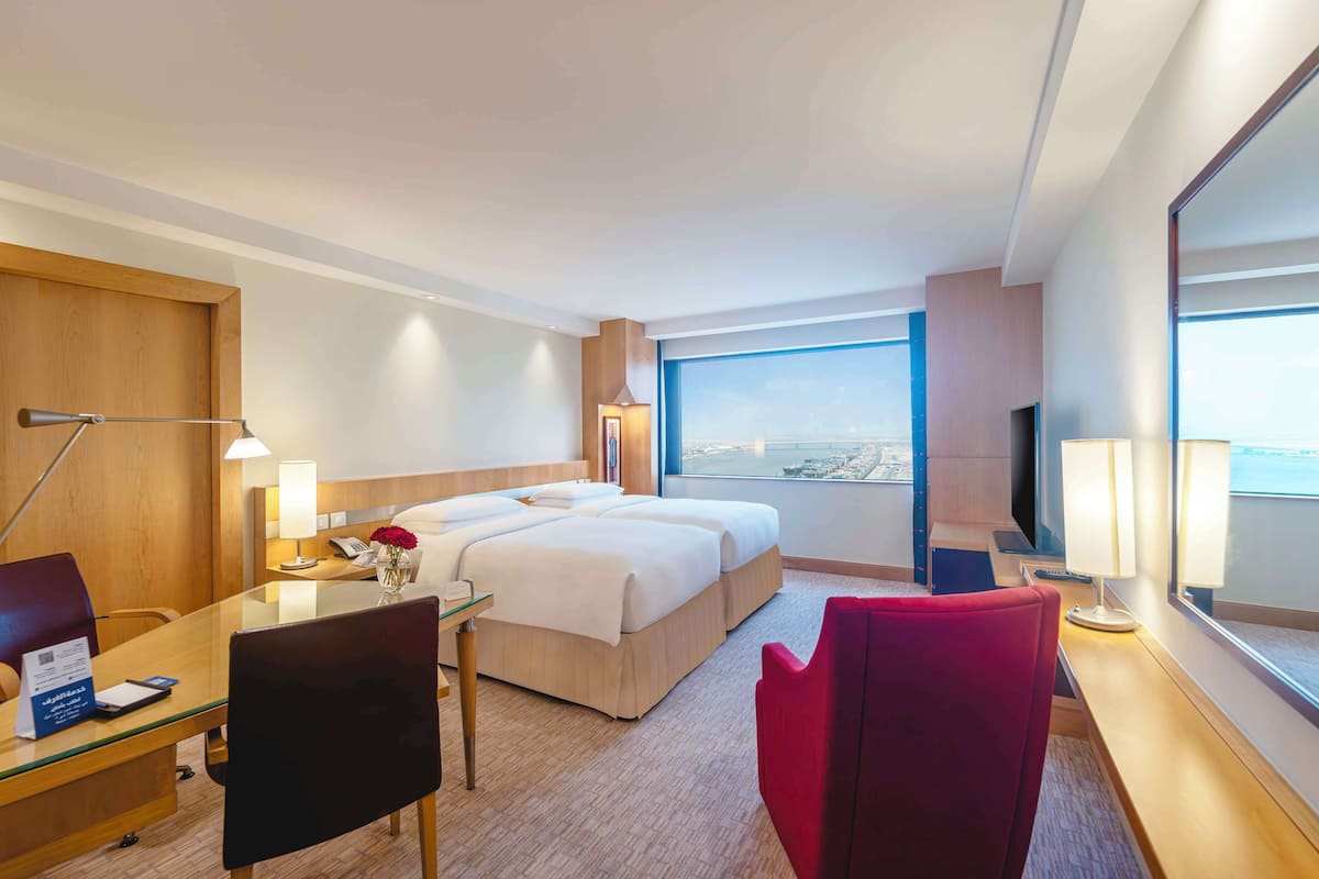 A hotel room with a large bed, a desk with a lamp, a chair, and a TV.