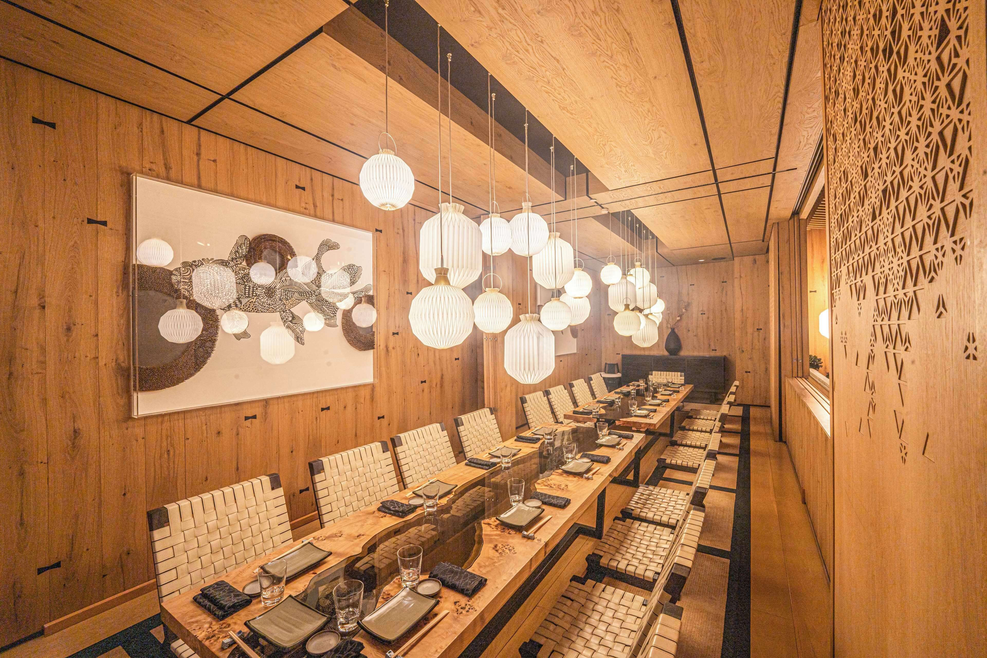 Uma longa mesa de jantar com várias cadeiras, paredes de madeira e luminárias esféricas penduradas.
