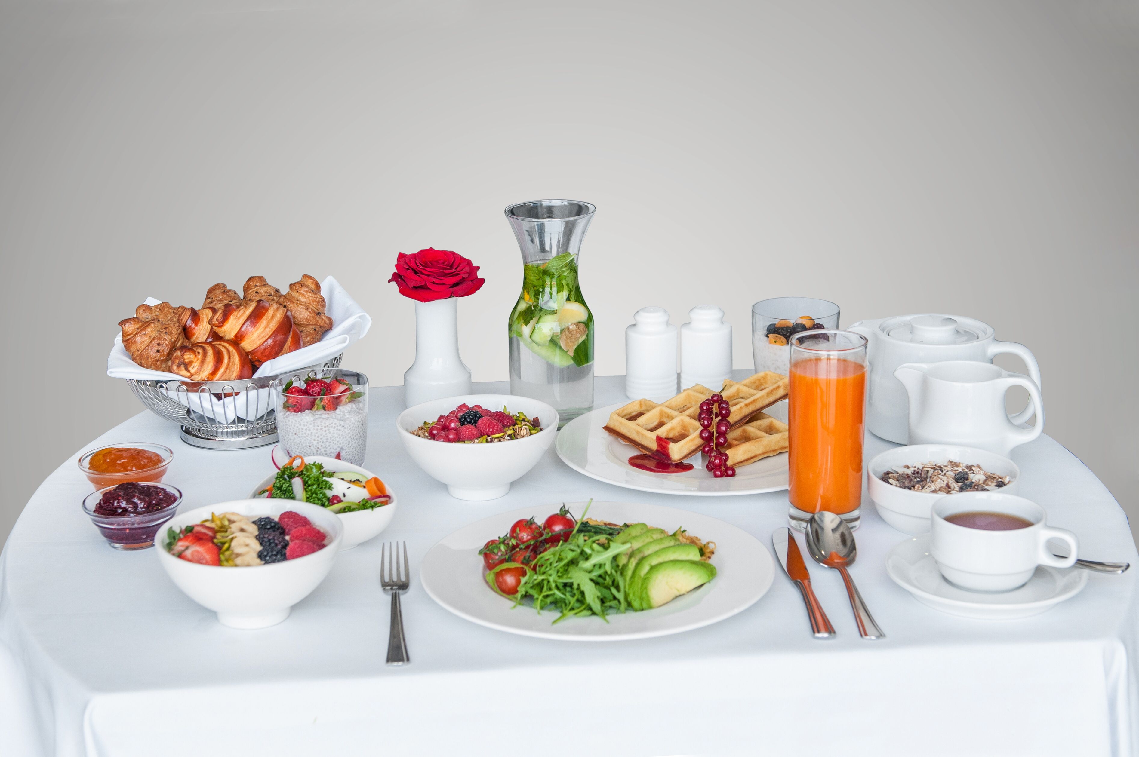 A breakfast table with various dishes, including waffles, a bowl of fruit salad, and a glass of orange juice.
