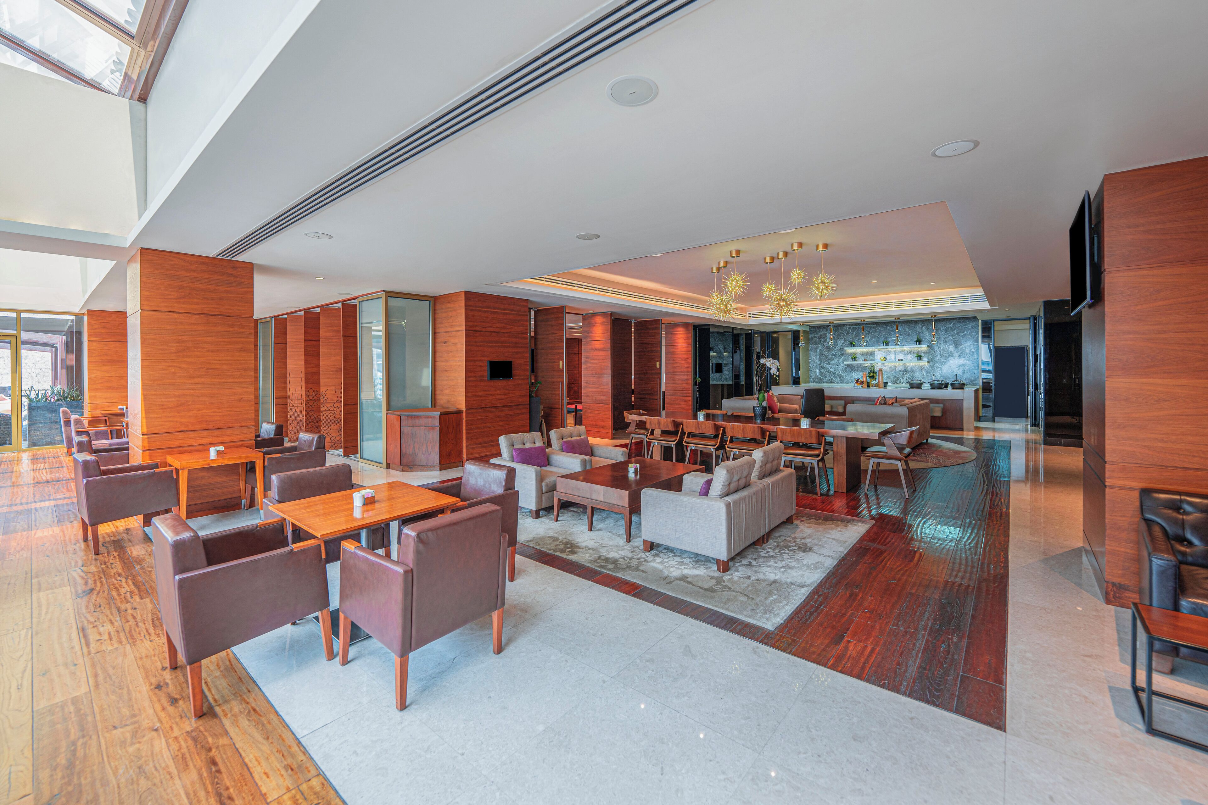 A spacious lobby with a mix of seating areas, a bar, and a kitchen visible in the background.