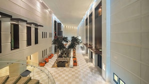 Um hall amplo com piso xadrez, áreas de estar, palmeiras e uma escadaria.