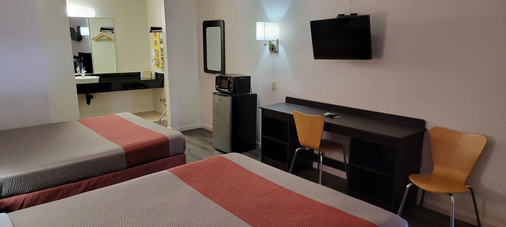 A hotel room with two beds, a desk, a chair, a TV, and a mirror.