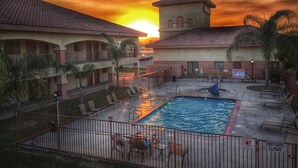 A hotel with a swimming pool, outdoor seating, and a view of the sunset. - Motel 6 Santa Nella, CA - Los Banos (Gustine)