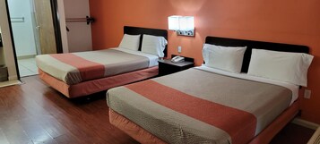Dos camas dobles con cabeceras y pies de cama a juego, una mesita de noche con lámpara, y una puerta que da a un baño.