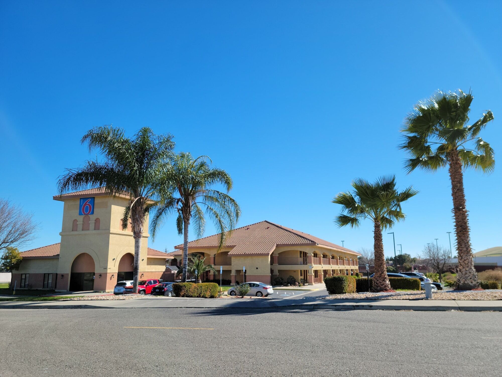 A hotel with a central tower, palm trees, and a parking lot.