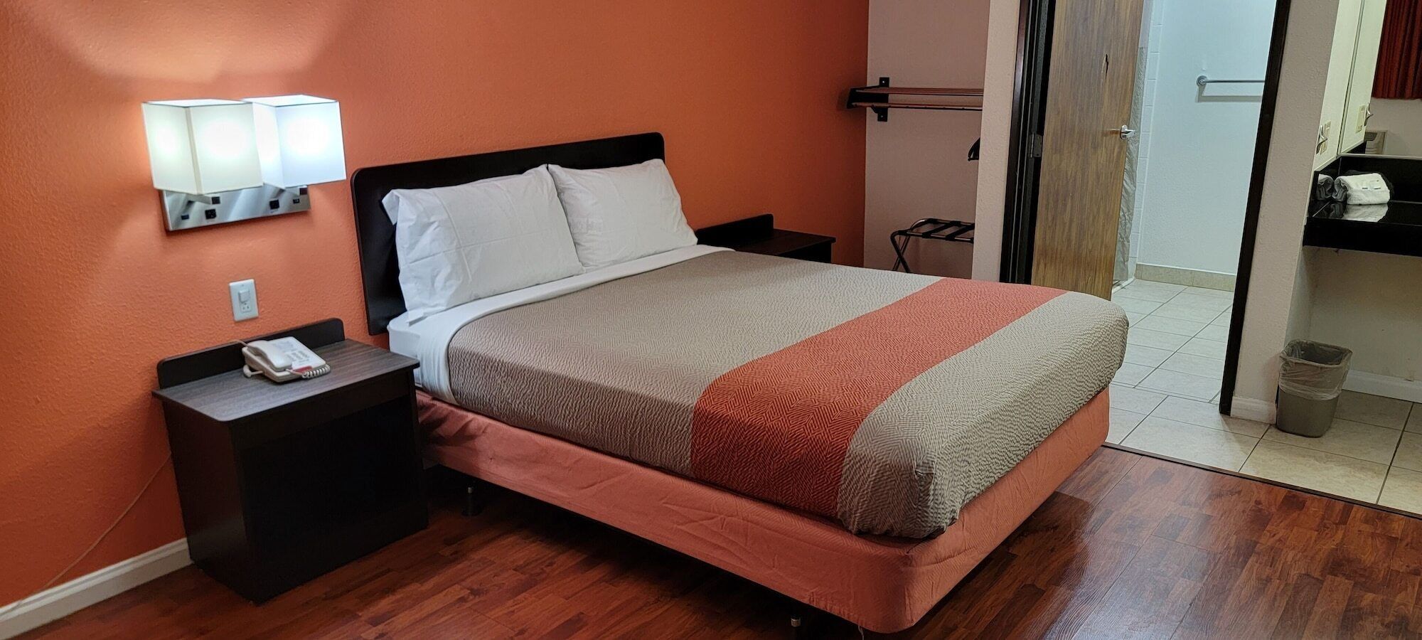 A hotel room with a bed, a bedside table with a phone, and a wall-mounted light fixture.