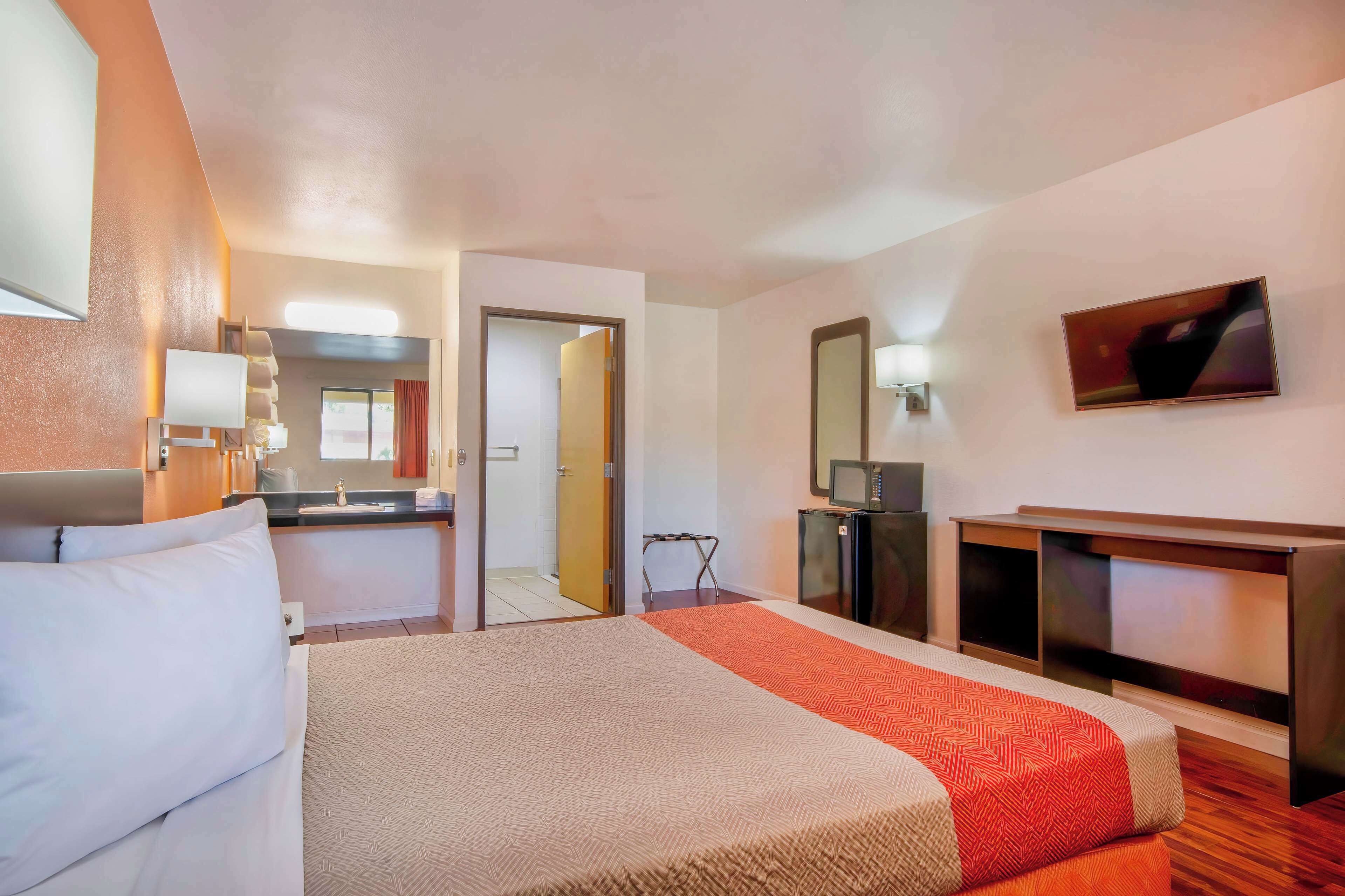 Une chambre d’hôtel avec un lit, un bureau, une télévision et une salle de bain visible à travers une porte ouverte.