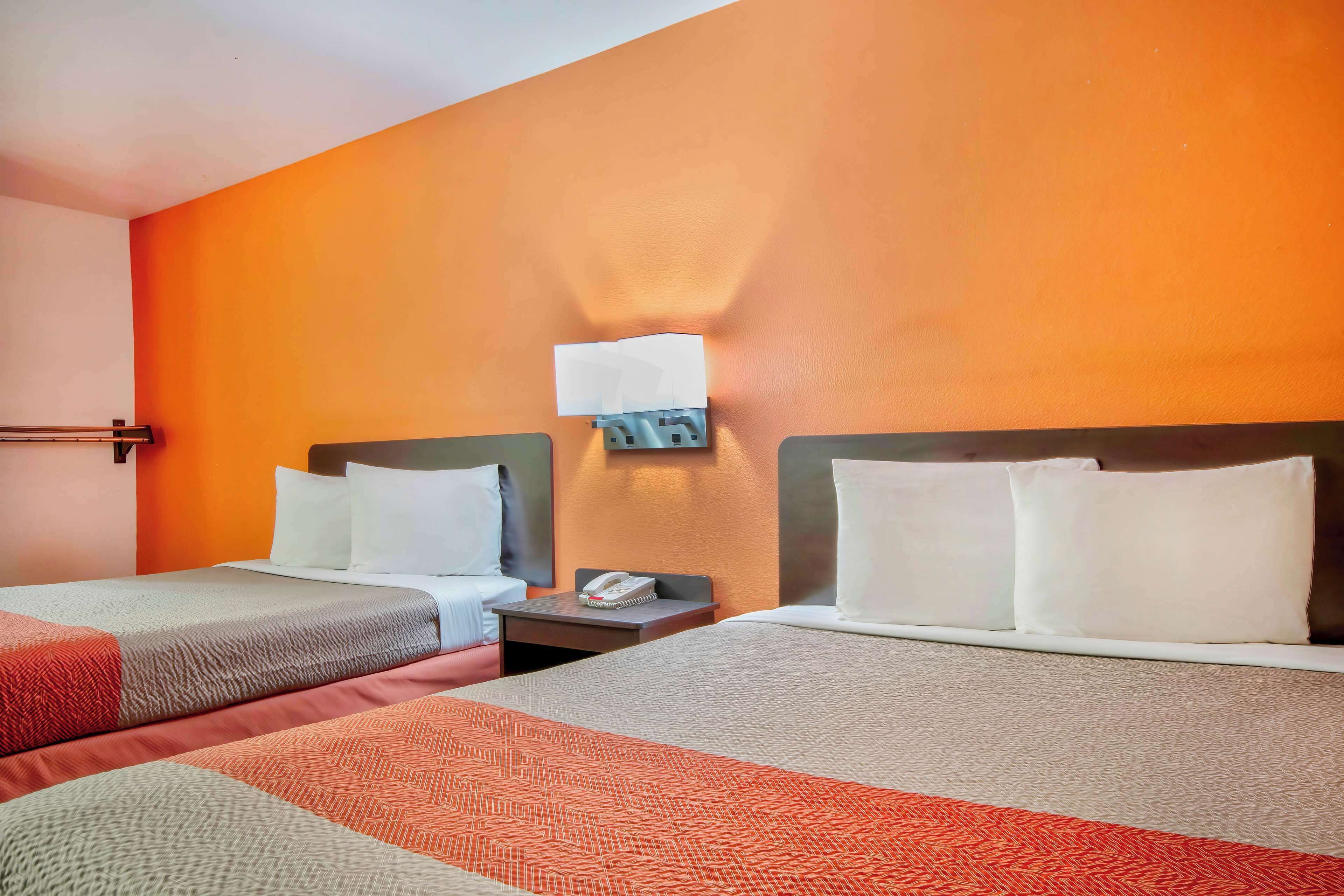 Una habitación de hotel con dos camas, una mesita de noche con teléfono y una lámpara fijada a la pared.
