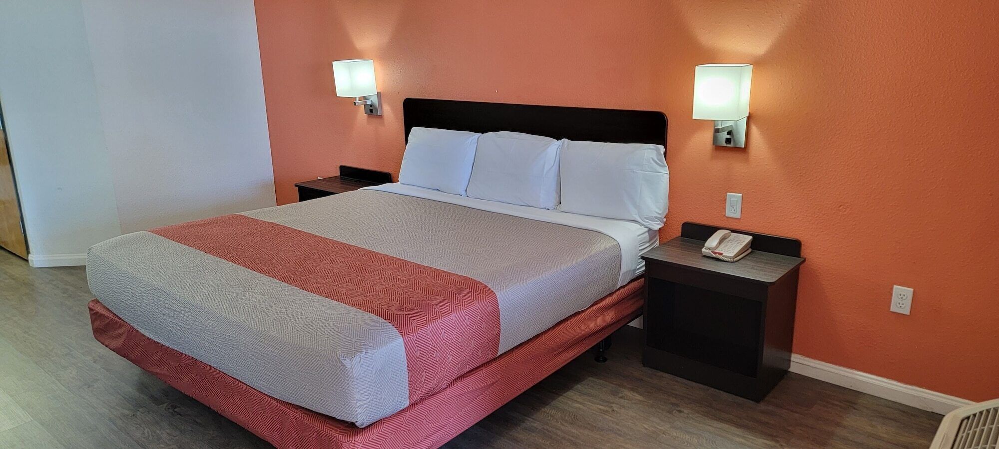 Una habitación de hotel con una cama, dos mesitas de noche y una mesilla con teléfono.