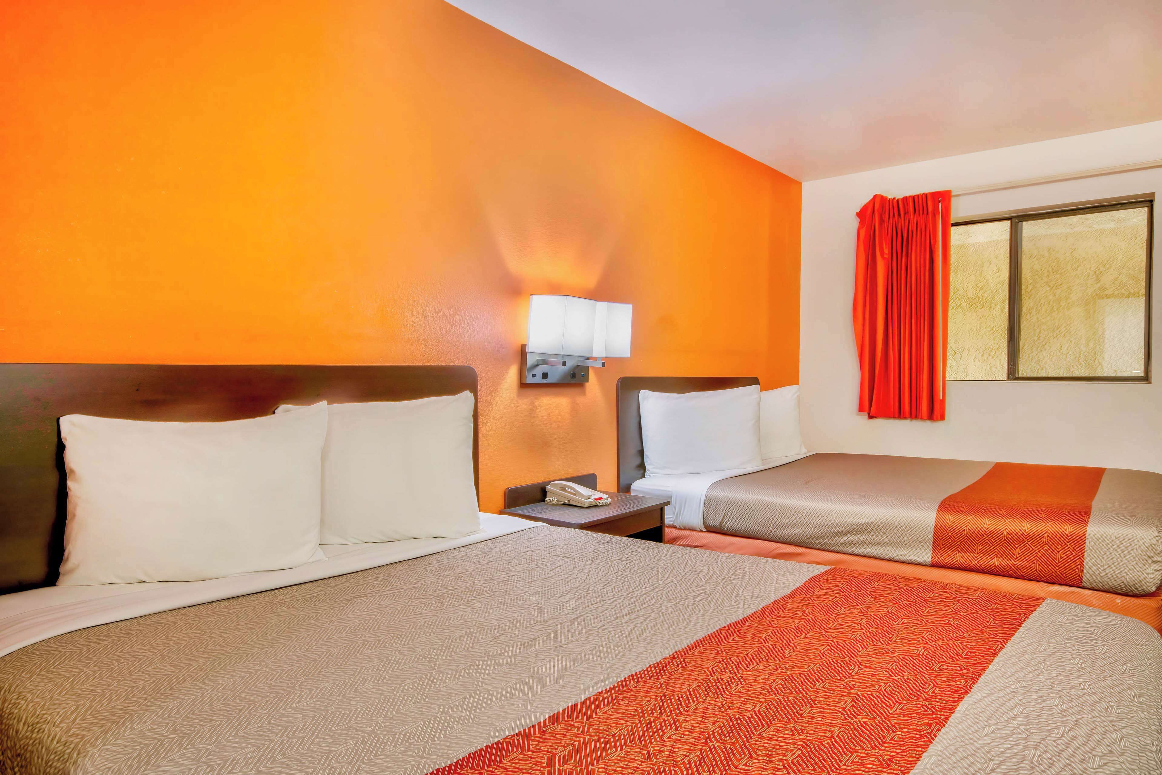 Habitación de hotel con dos camas, una mesita de noche, una lámpara y un ventanal con cortinas.