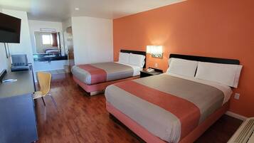 A hotel room with two beds, a desk, a chair, a TV, and a bathroom visible in the background.