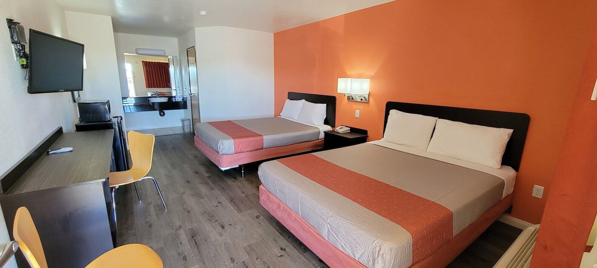 A hotel room with two beds, a desk, a chair, a TV, and a bathroom visible in the background.