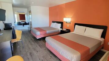 A hotel room with two beds, a desk, a chair, a TV, and a bathroom visible in the background.