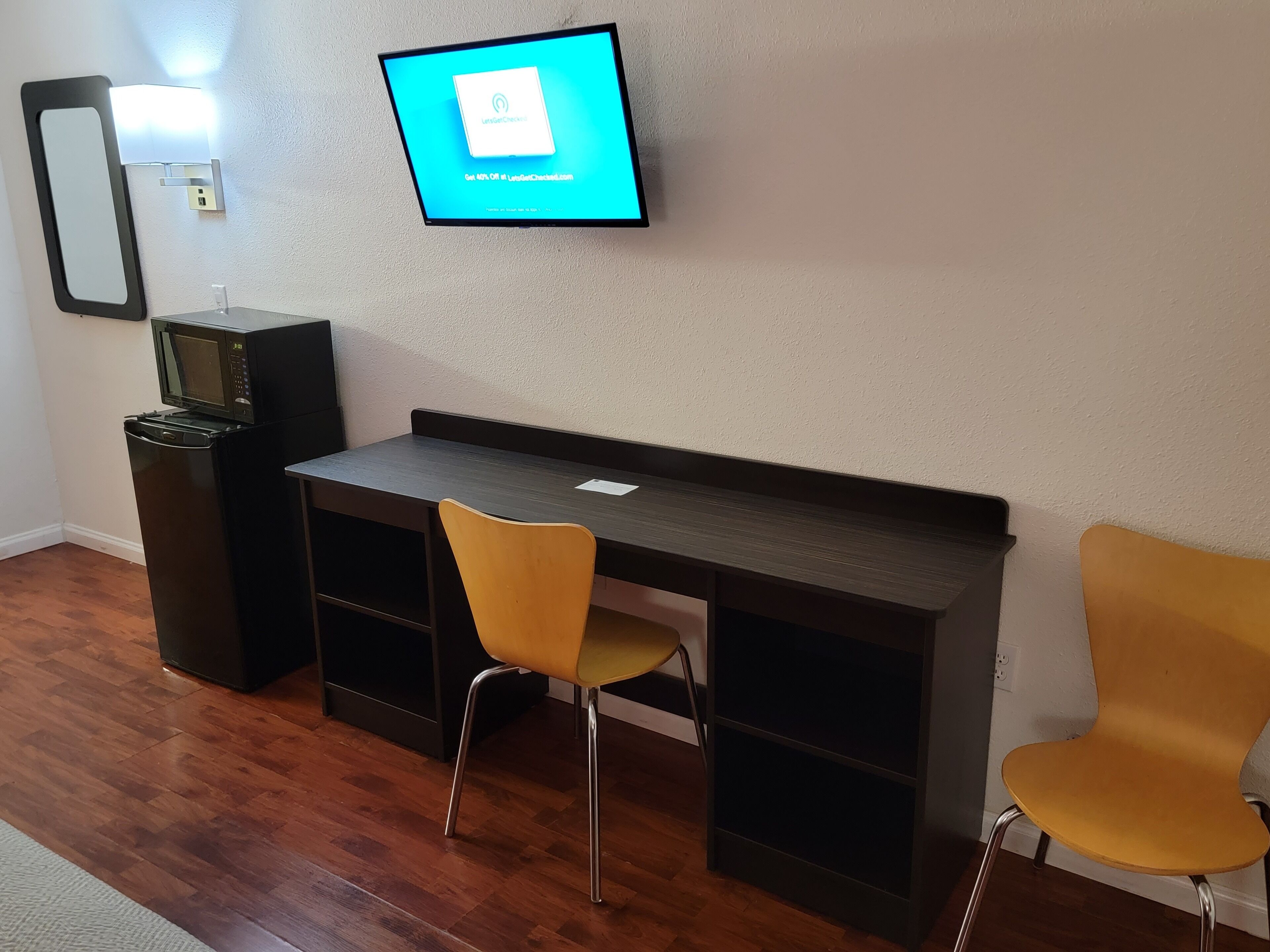 A modern room with a desk, two chairs, a television mounted on the wall, a microwave, and a small cabinet.