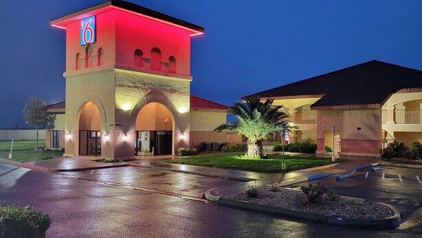 A hotel with a prominent tower featuring a neon sign, a well-lit entrance, and a parking lot. - Motel 6 Santa Nella, CA - Los Banos (Gustine)