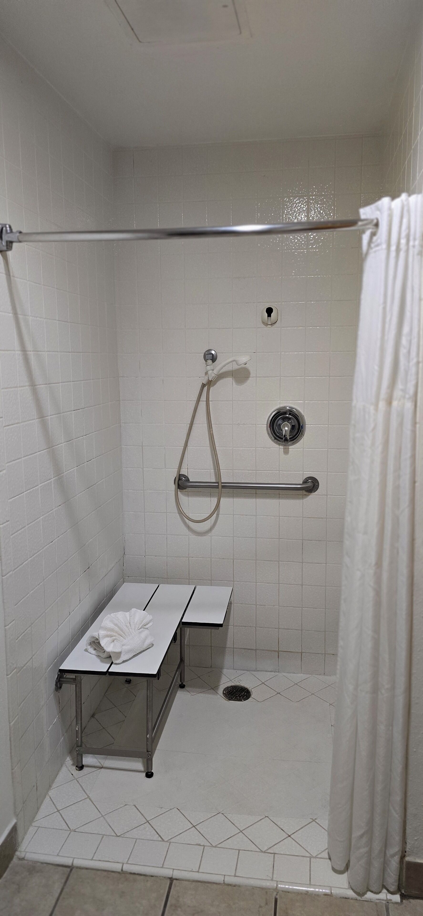 A small, white-tiled shower stall with a grab bar, a towel rack, and a showerhead.