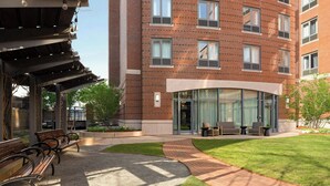 A brick building with a covered outdoor seating area, a grassy lawn, and a pathway. - Courtyard by Marriott Boston Brookline (Brookline)