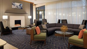 A modern living room with a fireplace, comfortable seating, and a large window. - Courtyard by Marriott Boston Brookline (Brookline)