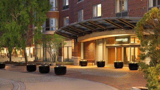 A brick building with a courtyard, potted plants, and a bench. - Courtyard by Marriott Boston Brookline (Brookline)