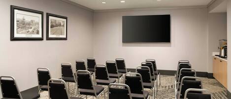 A conference room with rows of chairs, a flat-screen TV, and two framed pictures on the wall.