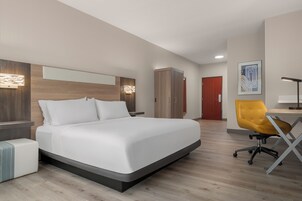 Una habitación de hotel moderna con una cama grande, un escritorio con una silla, un armario y una puerta.