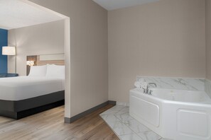 A modern bedroom with a large bed, a separate bathroom with a bathtub, and a wooden floor. - Holiday Inn Express & Suites Southfield Detroit by IHG (Southfield)