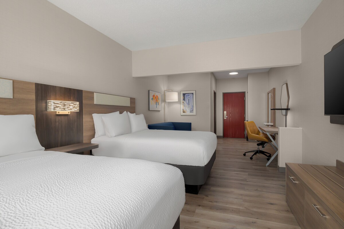 A hotel room with two beds, a desk, a chair, and a TV.