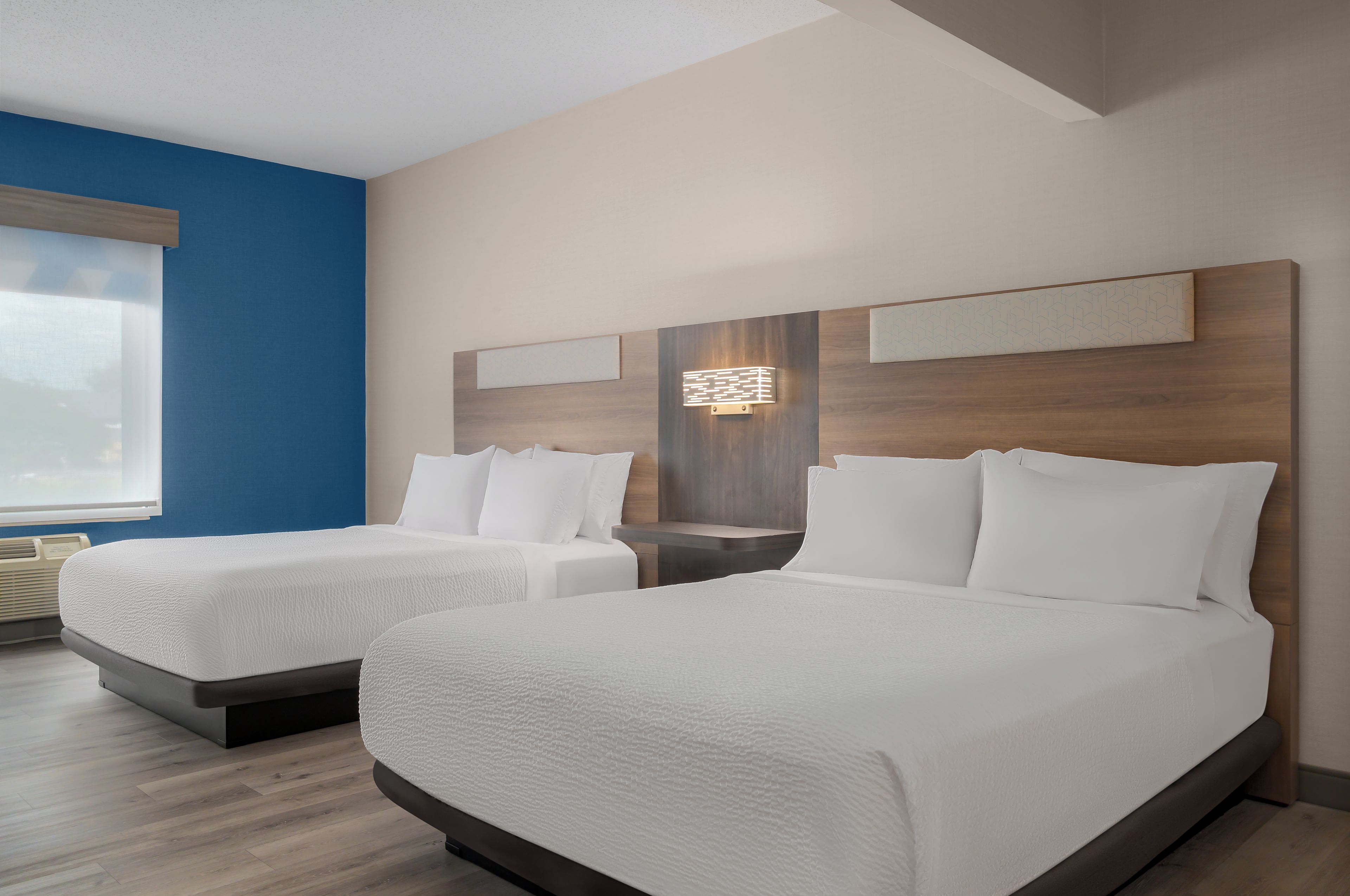 Habitación de hotel con dos camas, un ventanal grande y una lámpara fijada a la pared.