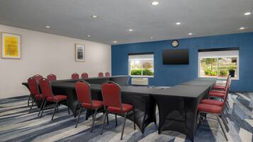 A conference room with a long table, red chairs, a clock, and a window with a view.